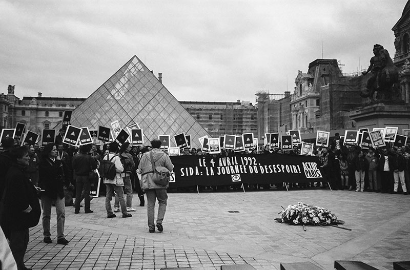 Crowd gathered outside the Louvre in Paris, with placards about AIDS