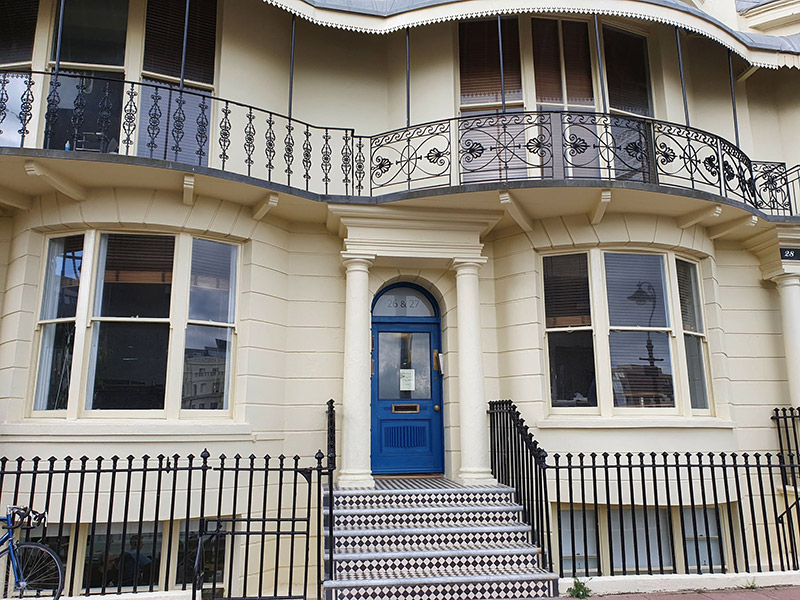 Front of building with a basement level, steps up to the front door and a balcony on the first floor