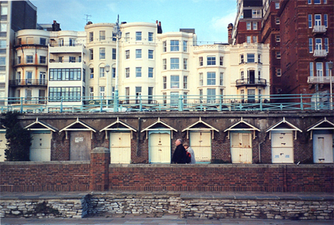 Two people walking past beach huts