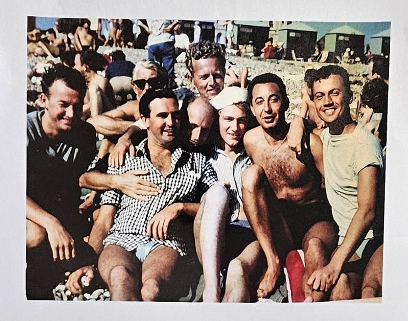 Group of men sitting closely in swimwear, on a beach