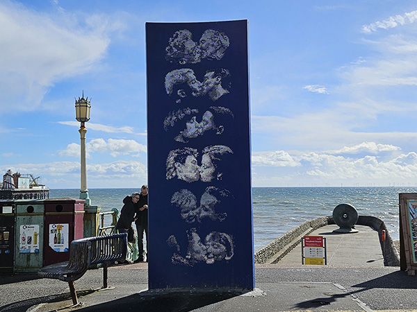 Vertical metal panel with holes in it, revealing 6 diverse couples kissing. 