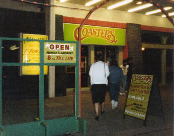 Two people entering a building at night with the sign Coasters lit up above the door